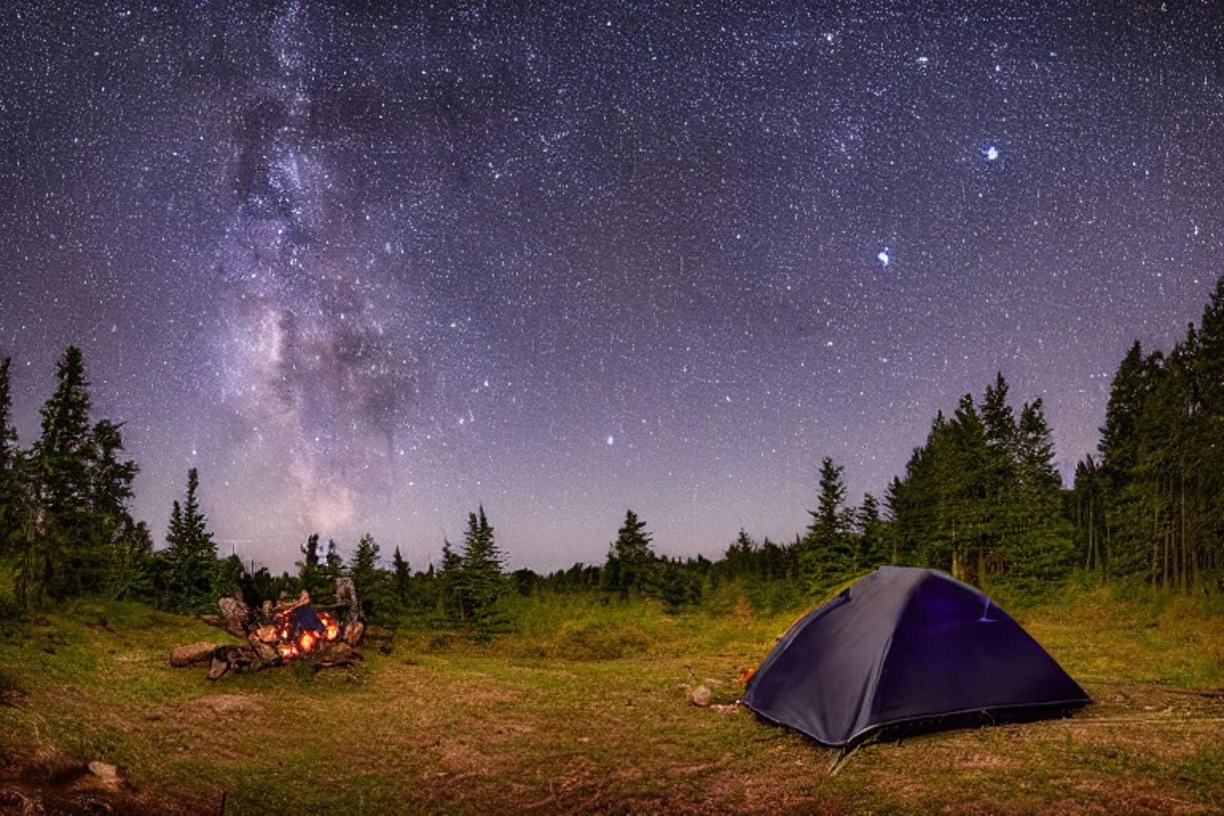 A black tent rests beside a quiet river under a starry, cloudy sky. In the center, a warm campfire glows among stones and logs on the dirt ground.