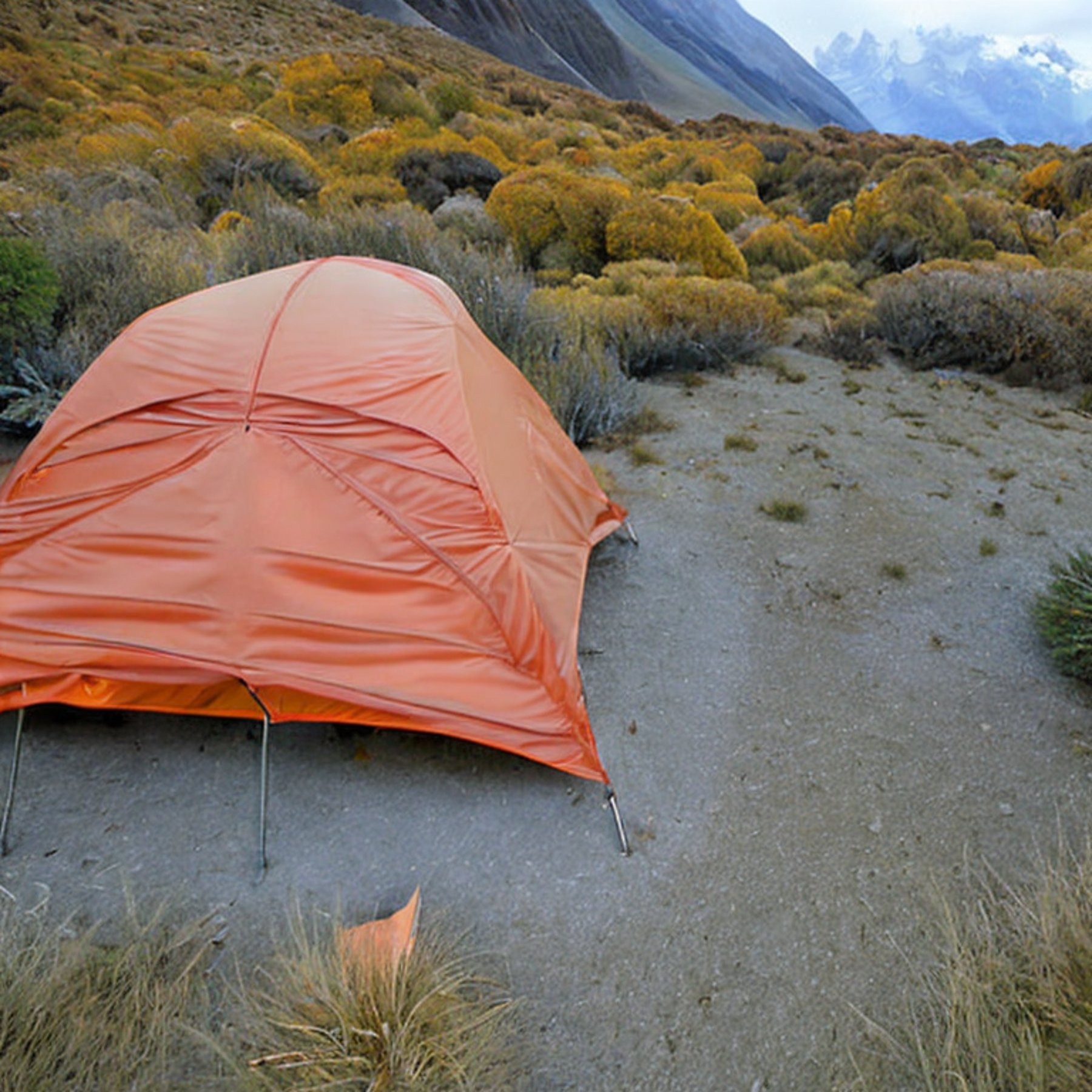 A gray and orange tent rests on a rough dirt clearing beneath the starry night sky. A warm campfire glows nearby, while large bushes and fall-colored trees surround the campsite. Mountains rise in the distance, with a parking spot close by.
