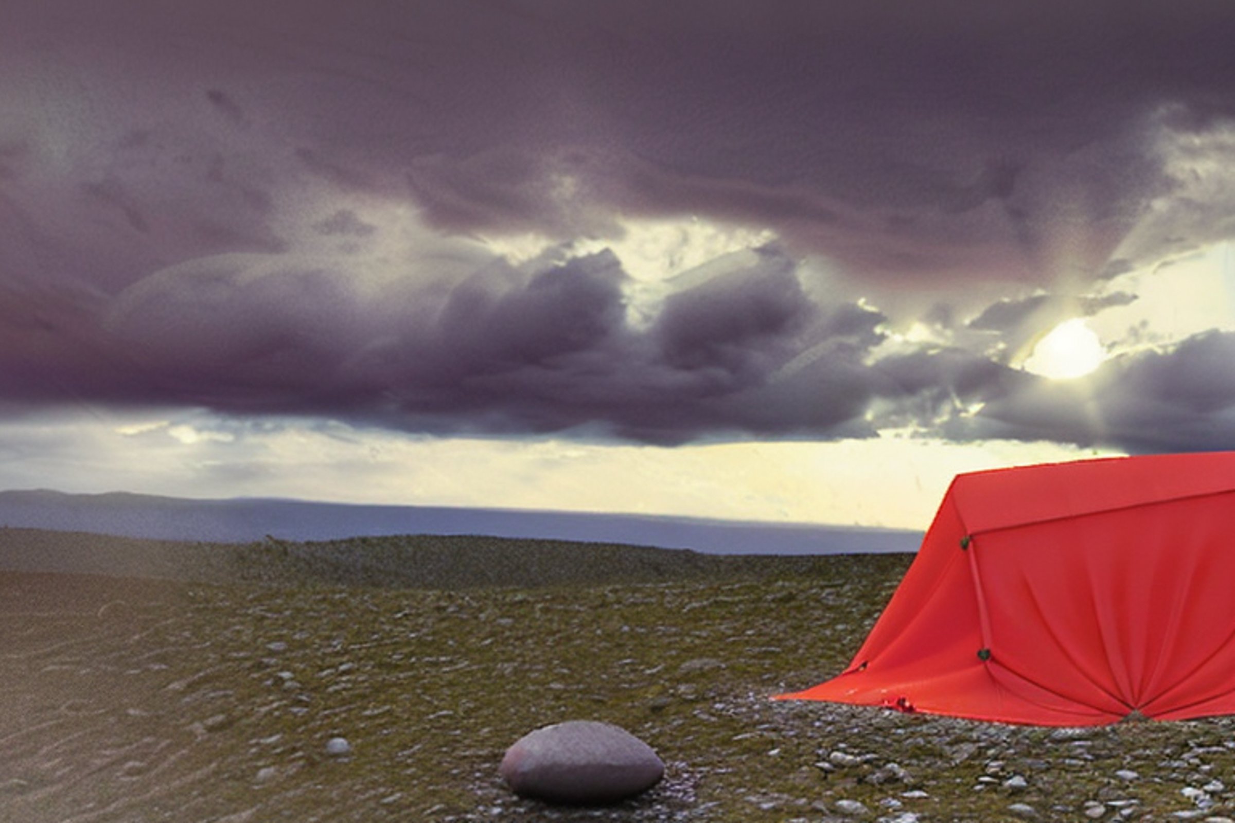 A bright red tent rests on a rocky mountain campsite as the sun sets beneath stormy clouds. A picnic table and clothesline add a cozy touch to the rugged landscape.