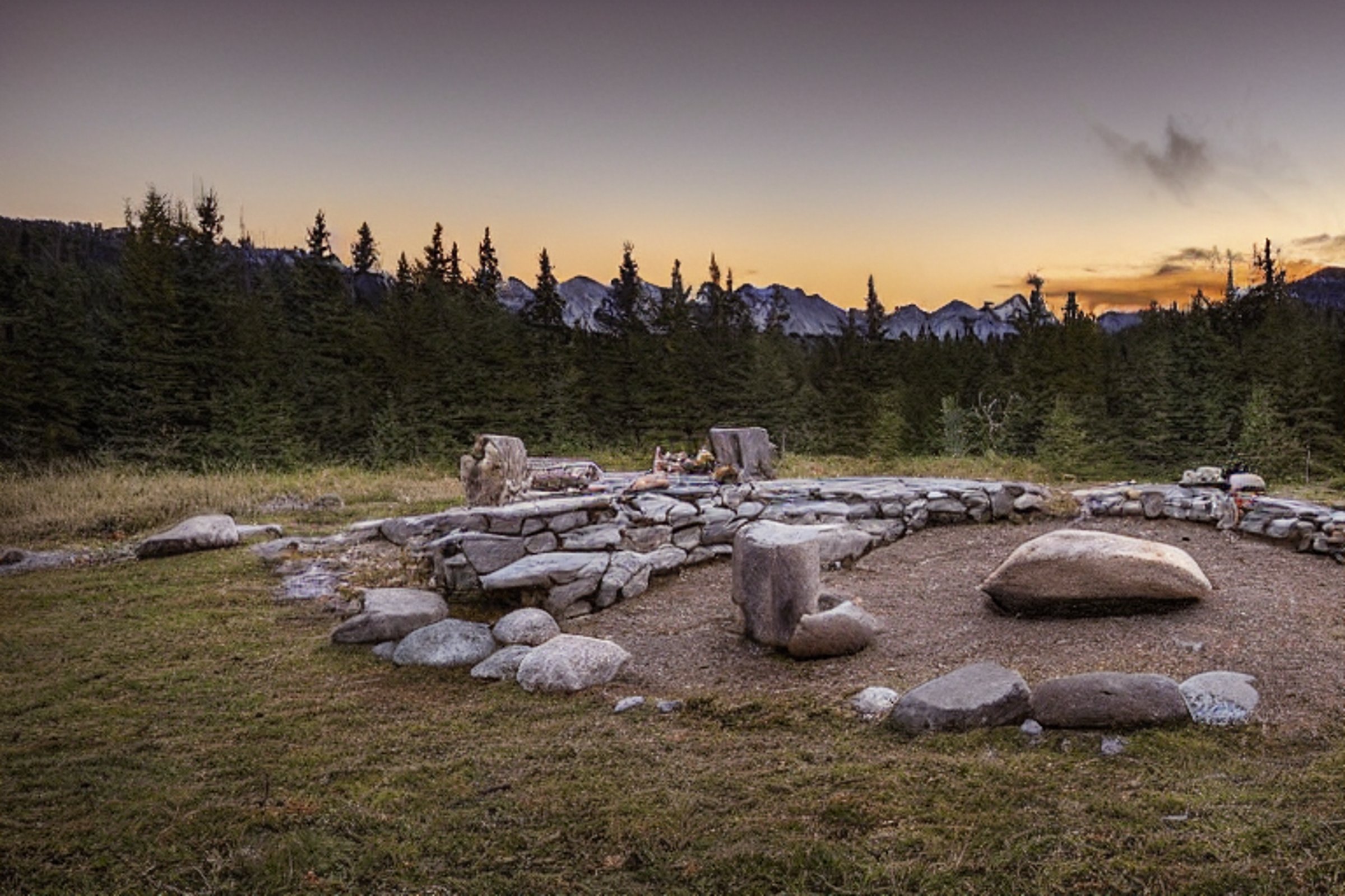 A teal tent rests on a snowy campsite beside a warm, steaming hot spring. A small campfire glows among the stones, while a deer stands quietly in the distance. Large rocks and stone slabs give the peaceful scene a wild, cozy feel.