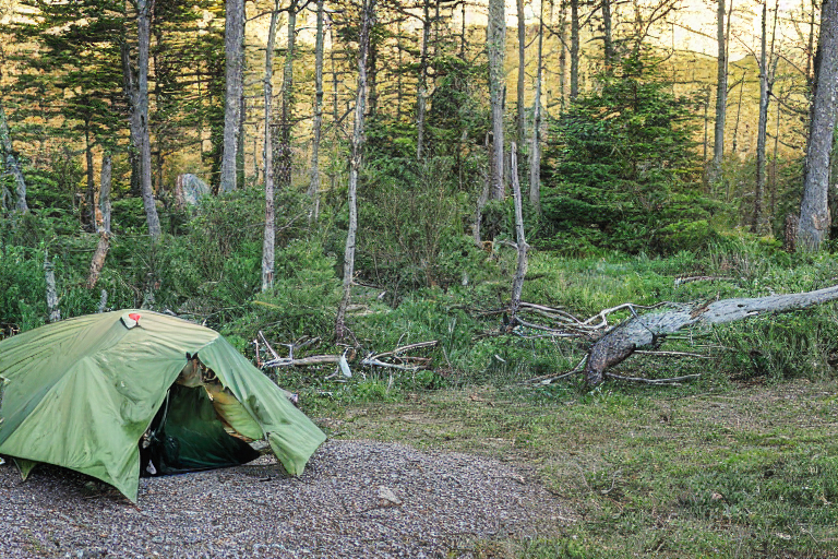A green camo tent rests beside a crackling campfire on Maine’s rocky coast. Clothes hang from a line as hikers gather nearby, with boulders and gravel scattered across the dirt. Stormy skies mix with warm golden light, creating a wild, cozy campsite.