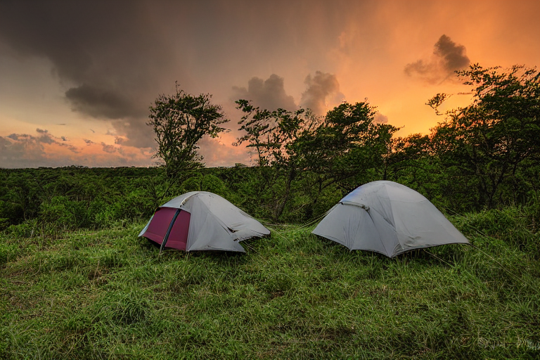 A cozy tent rests on a rocky dirt campsite as rain clouds gather over Biscayne National Park. Camping chairs sit nearby, while the sunset adds a soft glow to the rough landscape.