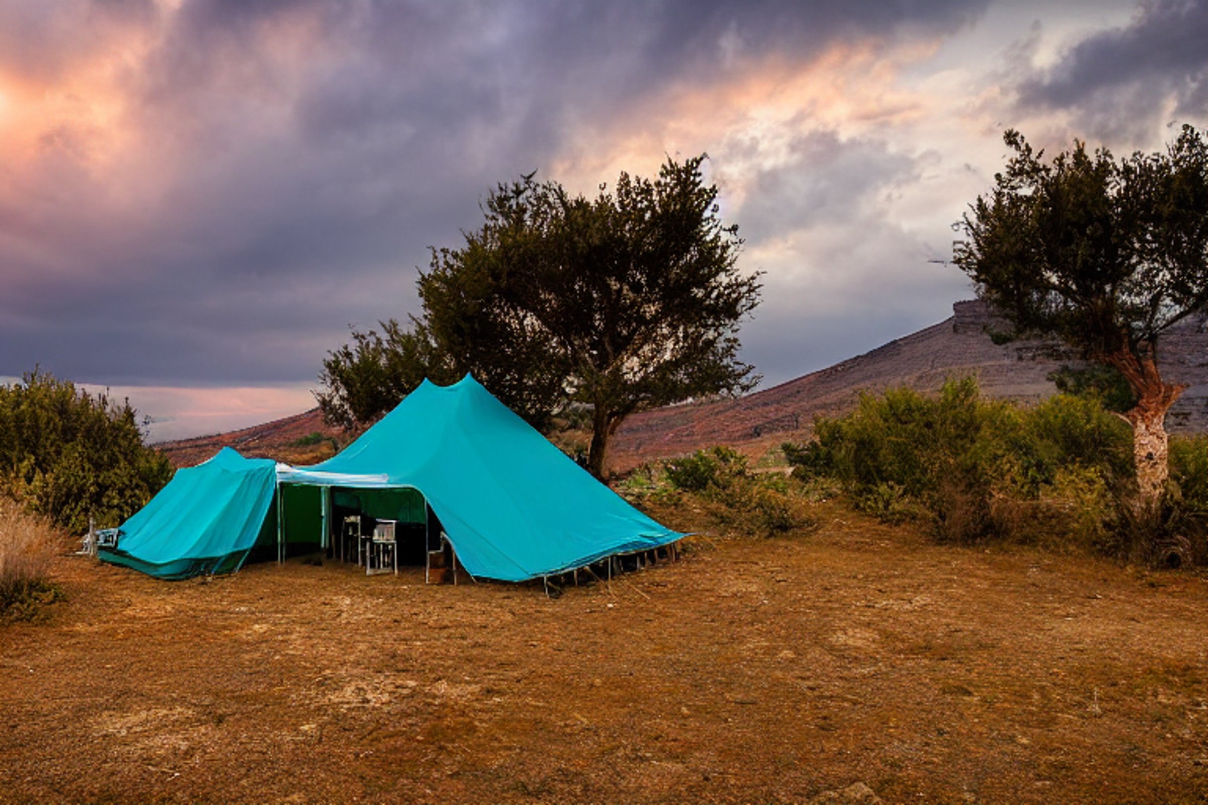 A teal tent rests on a quiet dirt patch as the sun sets over Santorini. Tall grass, large trees, and bright fall leaves surround the campsite, while hikers pass under a cloudy sky.