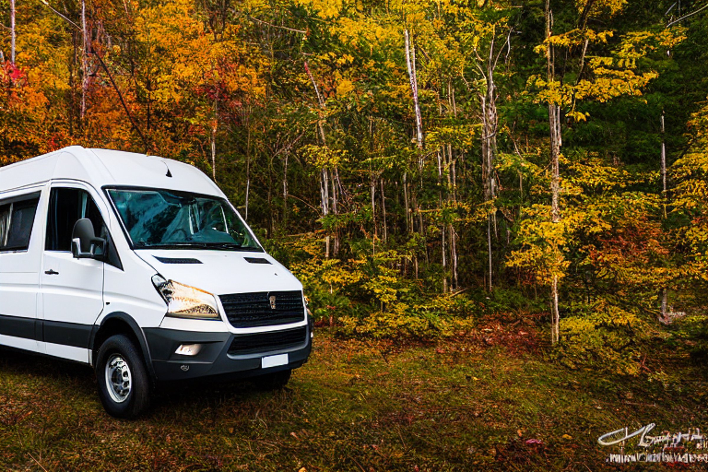 A white camper van rests at a quiet campsite in the Smoky Mountains. Snow dusts the ground as sunrise lights the rolling hills and bright fall trees. A camping lantern and gear box sit nearby, ready for adventure.