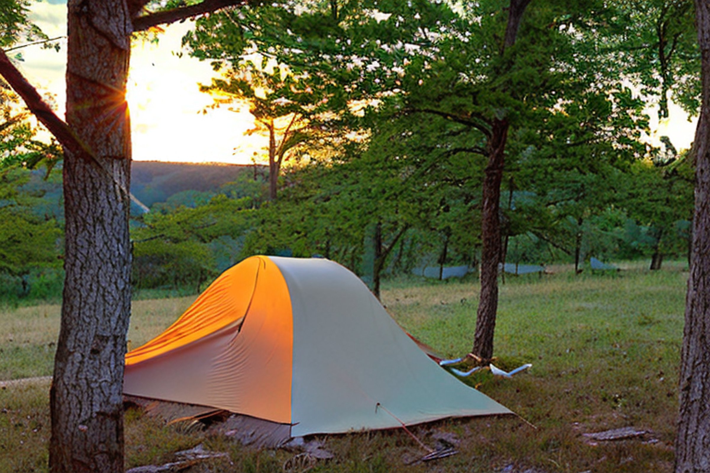 A cozy tent rests on a grassy Ozark campsite beside a small campfire. Rainy morning light shines through the trees, with a hammock, camping chairs, and a gear box nearby. A muddy dirt patch sits at the heart of the peaceful camp.