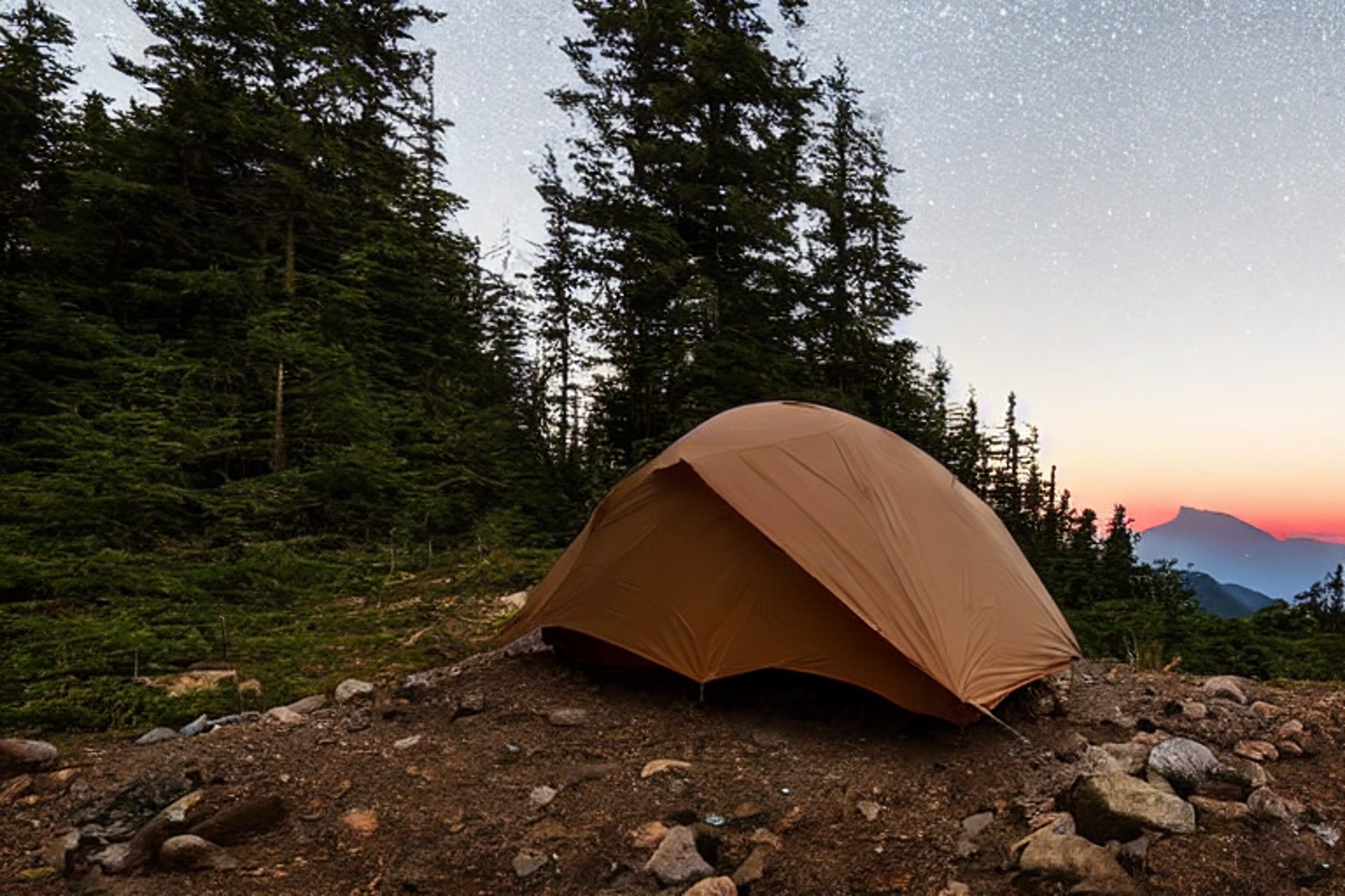 A brown tent rests on a quiet dirt campsite beneath a sky full of stars. Fog drifts around the mountain path, while a backpack sits nearby and the distant moon glows above the Smoky Mountains.