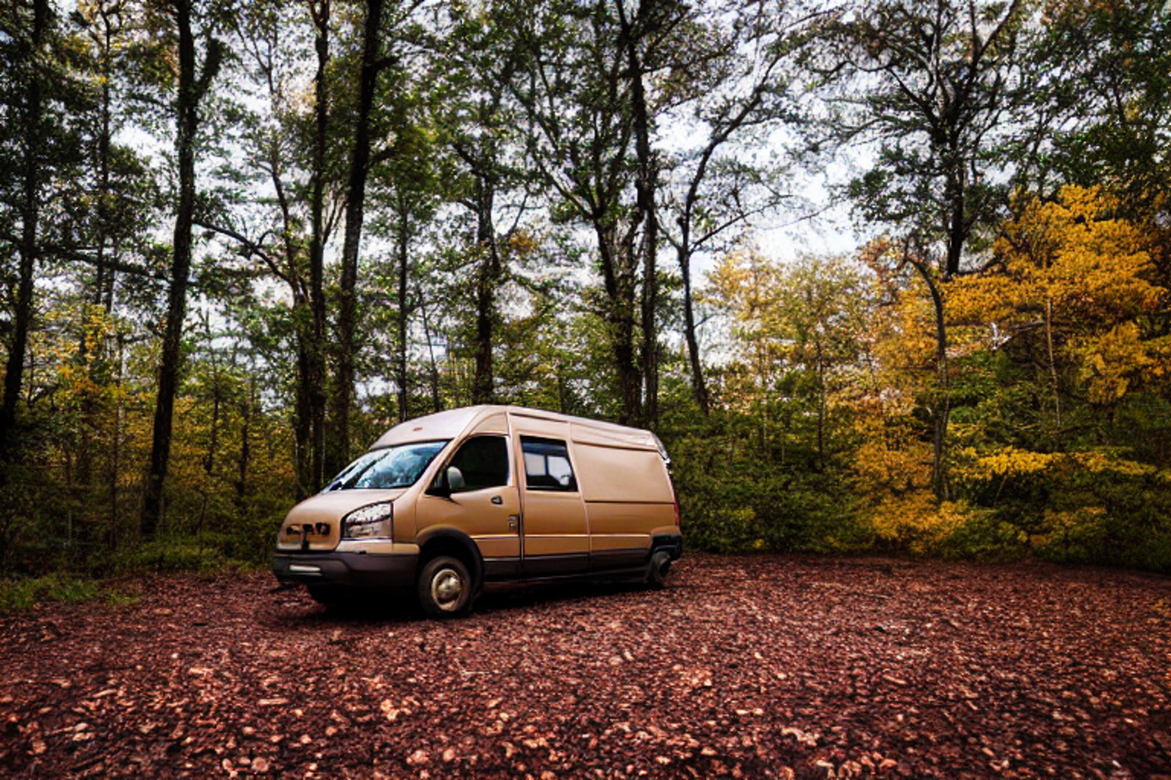 A brown camper van rests at a quiet campsite in the Ozark woods at dusk. Mossy trees glow with fall colors as storm clouds gather overhead. A warm campfire, logs, and a small lantern make the dirt clearing feel cozy.