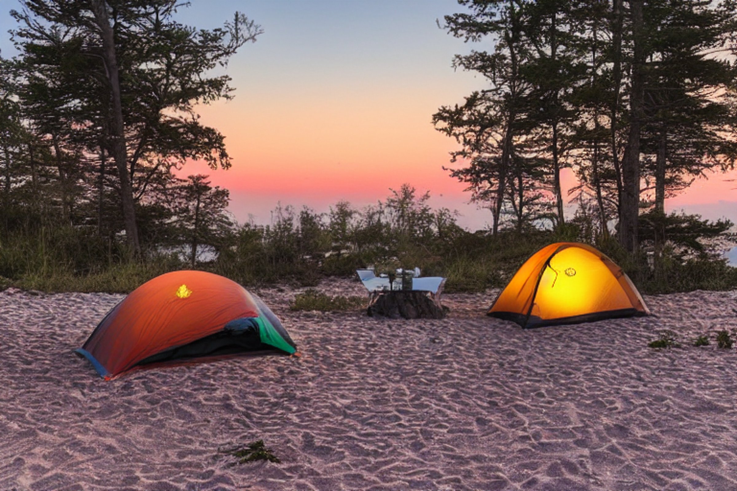 A colorful tent rests on a sandy beach beside a warm campfire. Boulders and small trees frame the campsite, while the ocean stretches beneath a cloudy sunset sky. A pale moon glows in the distance.