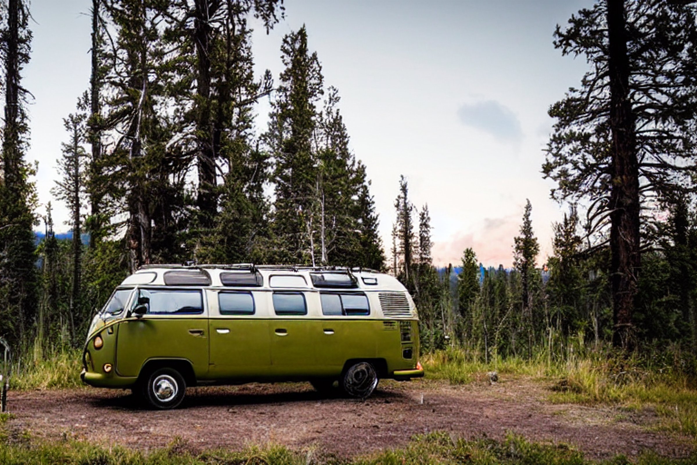A green camper van rests in a quiet Yellowstone campsite beneath a sky full of stars. A warm campfire glows beside a large log, while a hammock hangs between the trees. A clear stream runs through the peaceful dirt clearing.