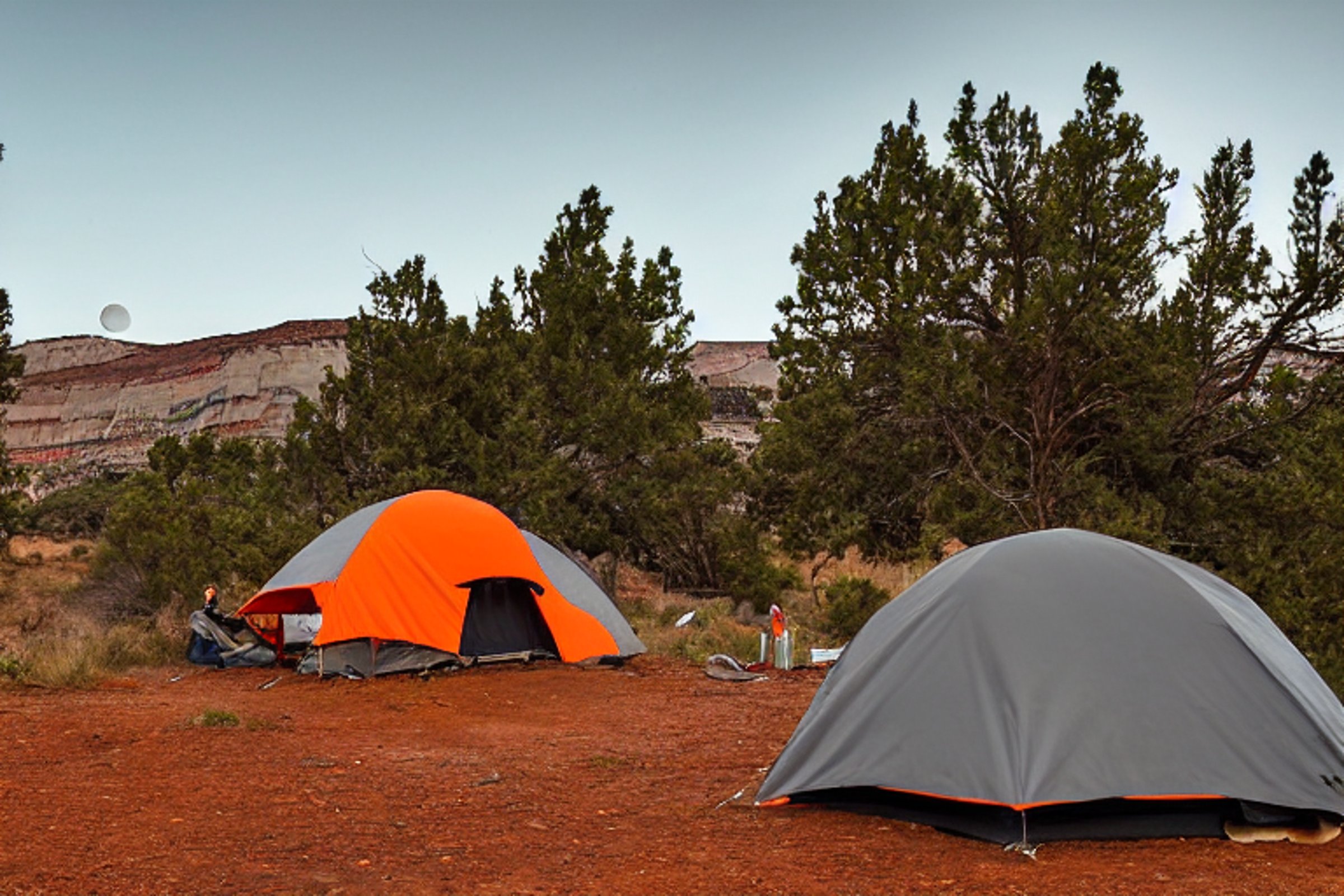 A gray and orange tent rests beside a dirt patch at a paved campsite in Capitol Reef National Park. Tall trees, cloudy skies, distant surfers, and a wooden guitar create a peaceful yet playful scene, with the moon faintly visible above.